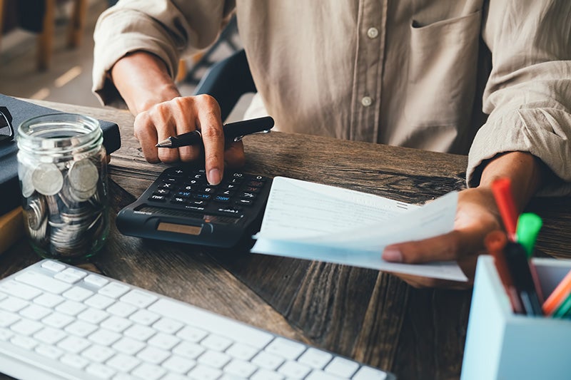 Person using a calculator with one hand and holding a paper in the other hand